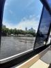 Rzeka płynąca przez miasto Brisbane w Australii oraz nabrzeże z ogródkami restauracyjnymi otoczone zielenią na tle błękitnego nieba widziane z okna łodzi motorowej. Na dalszym planie duże wieżowce.