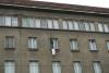 Fragment elewacji budynku archiwum. Jedno okno jest otwarte. Z okna powiewa transparent z napisem "Pomocy" na białym tle. Z okna wygląda mężczyzna.