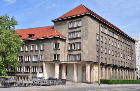 Trzypiętrowy, duży, szary stary budynek o prostych kształtach pokryty pomarańczową dachówką będący obecną siedzibą Archiwum Państwowego we Wrocławiu.