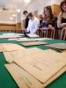 Grupa studentek i student stoją przy długim stole nakrytym zielonym obrusem w sali konferencyjnej archiwum. Na stole rozłożone są stare dokumenty w języku niemieckim. Studenic patrzą z zainteresowaniem na dokumenty leżące na stole.